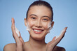 © Ilshat - Portrait of cheerful young asian ethnicity woman applying foam for washing on her face on a blue isolated. Lovely brunette with attractive appearance.