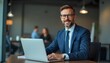 © Shams - Confident Professional: A distinguished businessman, radiating confidence, is captured at his desk, engrossed in work on a laptop, with a backdrop of blurred colleagues.
