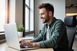 © MT - A Young Caucasian Male Working on a Laptop at a Bright, Modern Office Space, Smiling and Engaged in Productive Activity