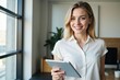 © MT - Young Caucasian Woman in a Light Blouse Holding a Tablet in a Modern Home Environment with Natural Light and Greenery