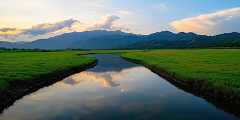 Aufkleber - A serene landscape featuring a tranquil river reflecting mountains and clouds, surrounded by lush green fields under a vibrant sky.
