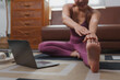 © Phimwilai - Young woman practicing online yoga class at home and stretching legs