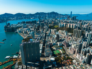 Poster - Aerial panorama of Hong Kong, China, showcases a dense cityscape with towering buildings meeting the coastline. Mountains rise in the distance under a clear blue sky.
