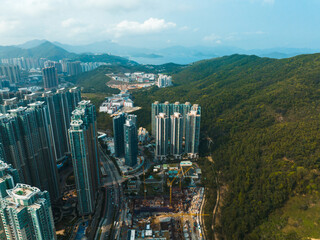 Poster - Aerial panorama of Hong Kong city showcasing dense buildings nestled between green mountains and blue water.  Urban landscape view from above.