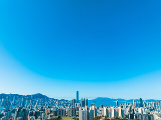Aufkleber - A wide aerial panorama captures Hong Kong city under a clear blue sky. Buildings stretch across the landscape with mountains in the background, offering a vast cityscape view.