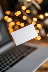 Poster - A blank business card is suspended above a laptop, illuminated by soft lighting. The background showcases a modern workspace with a sleek design, perfect for startups and digital branding