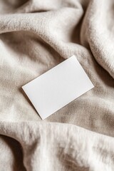 Poster - A blank business card rests on soft, textured linen, highlighting gentle folds and shadows. The warm background offers an earthy tone, ideal for eco-friendly branding and boutique aesthetics