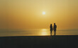 © DBFilms - A couple holding hands while watching the sunrise over the ocean. The golden hues reflect on the calm water, creating a romantic and peaceful moment.