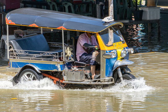 A traditional taxi motorized tricycle - tuk tuk drives through a flooded street, Bangkok, Thailand