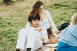 © qunica.com - A young couple sits closely on a picnic blanket, enjoying a sunny day outdoors. They are surrounded by food and share a moment of relaxation and connection on the grass.
