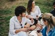 © qunica.com - A group of multiracial friends sharing food and wine during a picnic in nature. They are enjoying each other's company on a cloudy day, surrounded by greenery. A moment of relaxation and friendship.