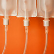© roberto - Close up of three IVs in a row, with drips, orange background. Care concept.