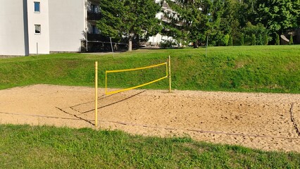 metal poles with a volleyball net for playing beach volleyball are set on a sandy area among grassy 