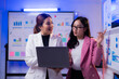 © Tj - Two asian businesswomen are discussing company strategy using a laptop and charts showing positive growth and success in a modern office meeting