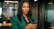 © Maxter Creative - An elegant professional in a green blazer uses her smartphone to connect with colleagues in a contemporary office with eco friendly plants.