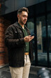 © dikushin - Vertical shot of stylishly dressed man standing on city street, using smartphone to check messages, browse internet, stay connected enjoying urban environment. Concept of urban lifestyle.