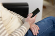 © Kateryna Muzhevska - An elderly man looks at his phone while sitting on the couch at home. He uses his smartphone to get current news, entertainment, and actively uses social networks.