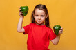 © Irina Mikhailichenko - Cute little girl in a red t-shirt on a yellow background, holding two green peppers and smiling. The child loves eco vegetables, concept of healthy child nutrition. Space for text, organic food
