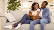© Prostock-studio - Beautiful african american lovers bonding on couch at living room while spending weekend together at home, copy space. Happy young black man and woman hugging and having pleasant conversation