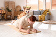 © Pixel-Shot - Sporty young redhead man with cute Corgi dog training on yoga mat at home