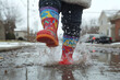 © AungThurein - A child wearing bright rain boots splashing into a puddle, with water droplets capturing the joy of rainy days