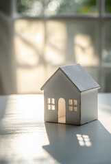 Poster - Charming White Miniature House Model with Reflections and Soft Natural Light Creating an Inviting Atmosphere for Home Decor Concepts