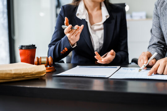 Two female lawyers in business suits meet at wooden desk, shaking hands over contract paper. wooden gavel and scales justice as discuss legal compliance, corporate law, dispute resolution.
