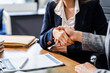 © Phushutter - Two female lawyers in business suits shake hands at wooden desk, finalizing legal agreement. wooden gavel and scales represent justice as they discuss corporate law, compliance, dispute resolution.