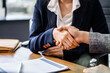 © Phushutter - Two female lawyers in business suits shake hands at wooden desk, finalizing legal agreement. wooden gavel and scales represent justice as they discuss corporate law, compliance, dispute resolution.