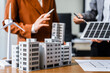 © Phushutter - Two businesswomen sit at a desk in a meeting, discussing property development while building a model of city tower. real estate investments, zoning laws, sustainable energy solutions. net zero