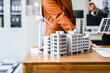 © Phushutter - Two businesswomen sit at a desk in a meeting, discussing property development while building a model of city tower. real estate investments, zoning laws, sustainable energy solutions. net zero