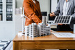 © Phushutter - Two businesswomen sit at a desk in a meeting, discussing property development while building a model of city tower. real estate investments, zoning laws, sustainable energy solutions. net zero