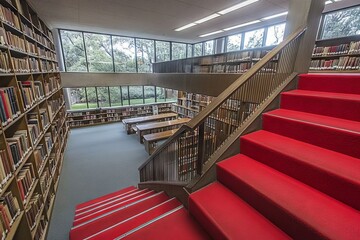 Poster - Library interior with red stairs and bookshelves showcasing a peaceful atmosphere and natural light during daytime hours