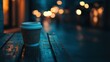 © yoga - Disposable coffee cup sits on a rustic wooden table at night, city lights blurred in background.