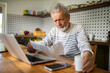 © Marko Geber - Senior man reading medication instructions while using laptop at home