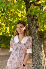 Poster - Woman in floral dress standing by a tree in Peterhof gardens during sunny afternoon
