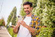 © deagreez - Young man enjoying outdoors using smartphone, dressed in casual checkered shirt, smiling in sunlight during urban walk