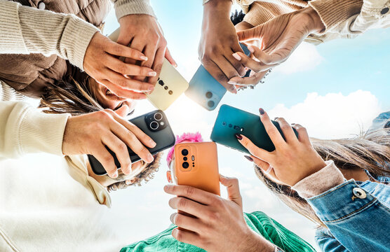 Group of young people using smart mobile phone device outside - Millenial women and men browsing on smartphone together - Trendy technology concept with guys and girls watching cellphone outdoors