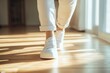 © scrdy - Person Wearing White Sneakers & Cuffed Jeans Walking on Wooden Floor in Light-Filled Room; Fashionable Casual Style