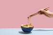 © Pixel-Shot - Female hand with chopsticks and bowl of ramen noodle soup on colorful background