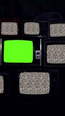 Wall Mural - remote turns on stack of tvs with static noise and central green screen - zoom-in - vertical 4k