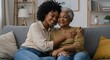 © Tiaga - Happy, hug and portrait of black woman with senior mother on sofa in home for womens day celebration together. Smile, bonding and African female person embracing mom for connection in living room.