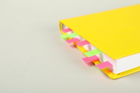 Book with colorful tabs on light gray background, closeup. Space for text