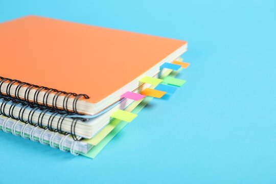 Notebooks with colorful tabs on light blue background, closeup. Space for text