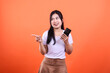 © Ajab - Young woman with smartphone pointing to the left isolated on an orange background
