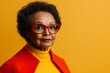 © ChaoticMind - Senior woman with stylish glasses poses against a vibrant yellow background in a colorful outfit