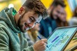 © whitestorm - A smiling young man intently drawing on a digital screen with a stylus, surrounded by a group of students in a collaborative, modern learning environment.