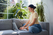 © baranq - Young woman working on laptop while sitting on sofa at home