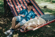 © qunica.com - Two young men enjoying leisure time in a hammock, relaxing under the shade of a tree in a park on a sunny day.