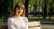 © Postmodern Studio - Caucasian young female in white blouse sitting on park bench in sunlit green park